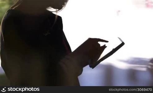 Tilt shot of a woman using tablet PC. Black silhouette against bright light