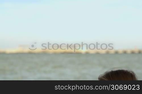 Tilt shot of a young woman in sunglasses typing on tablet computer sitting by the sea