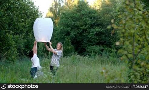 Tilt shot of mother with her children in the woods flying a fire lantern, which going high in the blue sky