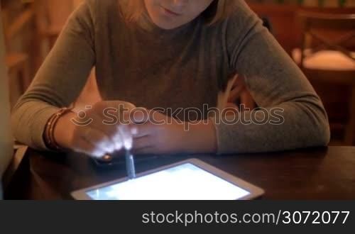 Tilt shot of young woman having quiet evening in a cafe. She drinking tea and working with tablet computer