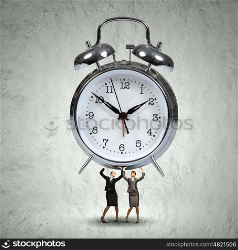 Time concept. Two businesswoman lifting huge alarm clock above head
