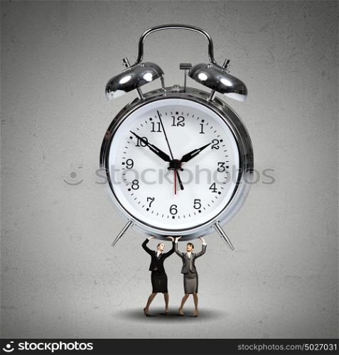 Time concept. Two businesswoman lifting huge alarm clock above head