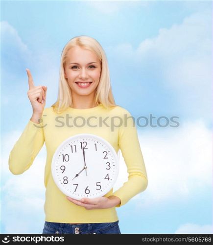 time, education and people concept - smiling young woman with wall clock showing 8 and finger up