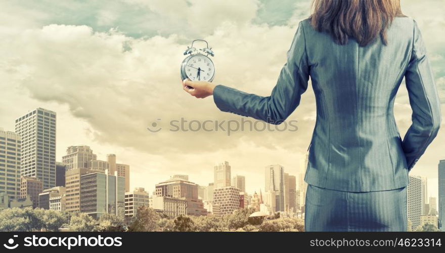 Time for business. Back view of businesswoman holding alarm clock against city background