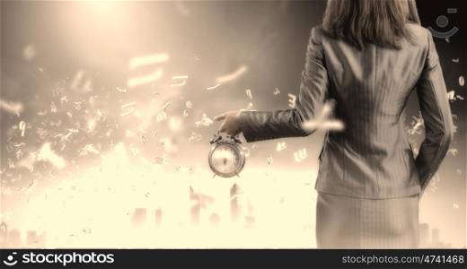 Time for business. Back view of businesswoman holding alarm clock against city background
