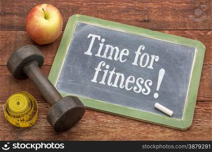time for fitness concept - slate blackboard sign against weathered red painted barn wood with a dumbbell, apple and tape measure
