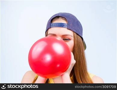 Time for party. Young trendy woman prepare birthday celebration decoration. Teenage girl in cap blowing red balloon.. Female teenager inflating red balloon.