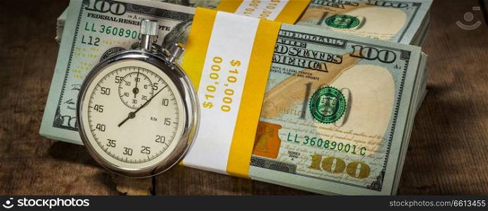 Time is money loan concept background -  letterbox panorama of stopwatch and stack of new 100 US dollars 2013 edition banknotes  bills  bundles on wooden background. Time is money