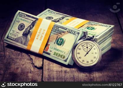 Time is money loan concept background. Vintage retro effect filtered hipster style image of stopwatch and stack of new 100 US dollars 2013 edition banknotes bills bundles on wooden background. Time is money