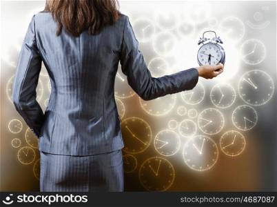 Time is passing. Rear view of businesswoman holding old alarm clock