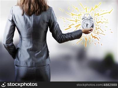 Time is passing. Rear view of businesswoman holding old alarm clock