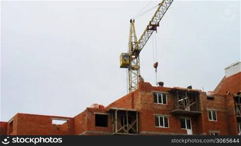 time-lapse construction activity, workers lay bricks, behind them rotated tower crane
