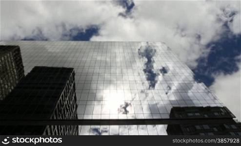 Time lapse, looking up at a glass-covered skyscraper, reflecting the blue sky, the passing clouds, and sun