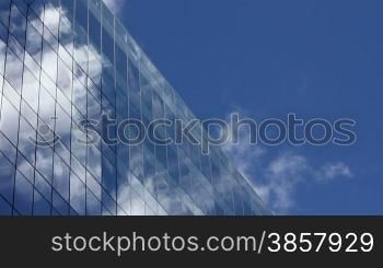 Time lapse, looking up at a glass-covered skyscraper, reflecting the blue sky and passing clouds