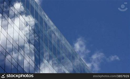 Time lapse, looking up at a glass-covered skyscraper, reflecting the blue sky and passing clouds
