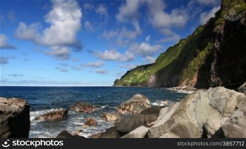 Time lapse of a rocky coastline line with steep foliage-covered cliffs in Hawaii, clouds rolling by overhead