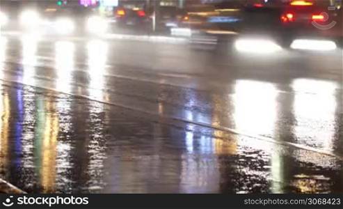 Time lapse of city traffic at night: cars with bright headlights moving on wet road.