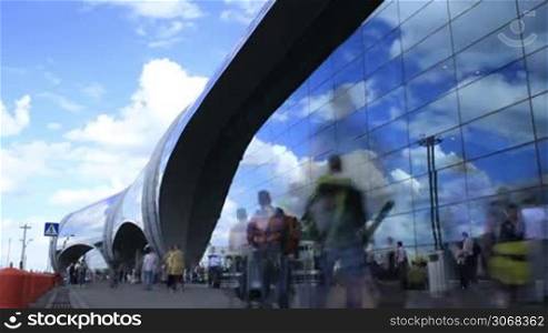 Time lapse of people walking fast near Domodedovo airport in Moscow. Running clouds reflecting in glassy surface of building.
