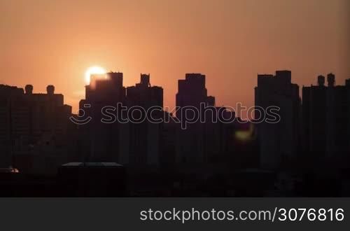 Time lapse shot of sun rising and moving in the sky, city modern buildings silhouettes on the foreground in red color. Seoul, South Korea