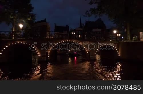 Time lapse view of night cityscape during river cruise on moving boat, buildings with lights, cars on the waterfront, Amsterdam, Netherlands