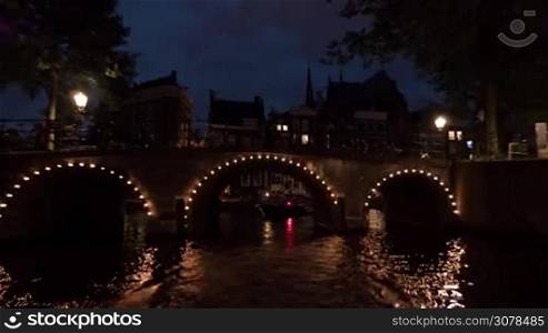 Time lapse view of night cityscape during river cruise on moving boat, buildings with lights, cars on the waterfront, Amsterdam, Netherlands