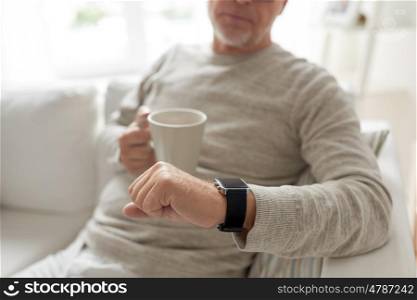 time, morning and people concept - close up of senior man with coffee or tea mug looking at wristwatch at home