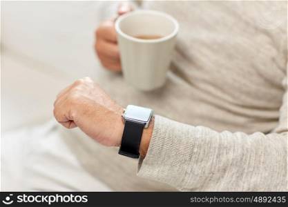 time, morning and people concept - close up of senior man with cup of tea looking at wristwatch at home