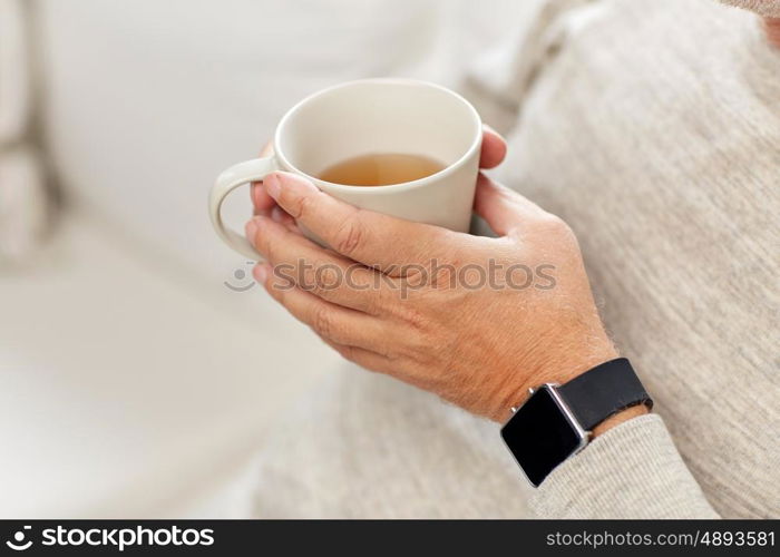 time, morning and people concept - close up of senior man with cup of tea and wristwatch at home