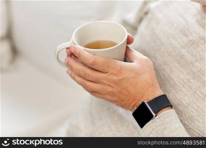 time, morning and people concept - close up of senior man with cup of tea and wristwatch at home
