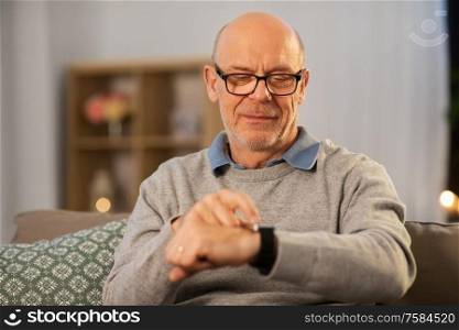 time, morning and people concept - senior man looking at wristwatch at home in evening. senior man looking at wristwatch at home