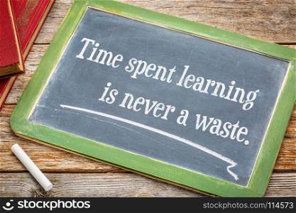 Time spent learning in never a waste - inspiraitonal quote on a slate blackboard with a white chalk and a stack of books against rustic wooden table