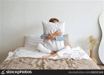Time to sleep, sleep deficiency, good morning concept. Teenager boy sitting on bed, embracing white pillow, hiding face behind. Minimalist scandinavian neutral bedroom interior, lifestyle.. Time to sleep, sleep deficiency, good morning concept. Teenager boy sitting on bed, embracing white pillow, hiding face behind. Minimalist scandinavian neutral bedroom interior, lifestyle
