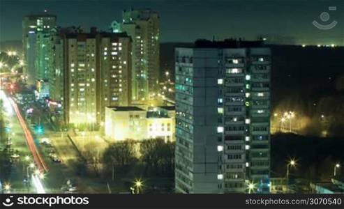 Timelapse and high angle shot of illuminated big city at night. Multistorey houses with window lights on and off and intense traffic