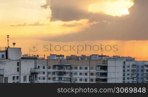 Timelapse and panning shot of golden sky during sunset with moving and transforming clouds over the multistorey houses in the city