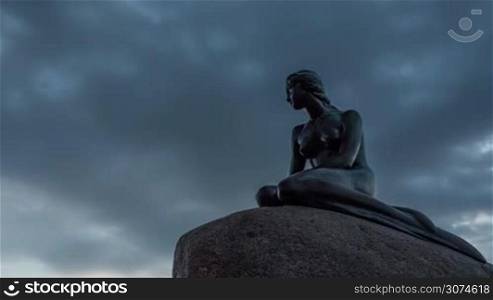 Timelapse low angle shot of clouds sailing over the famous bronze statue of the Little Mermaid in Copenhagen, Denmark