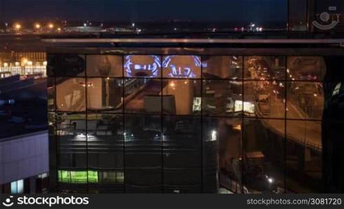 Timelapse night shot of city and car traffic reflecting in the glassy facade of modern building, airport in background