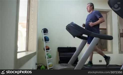 Timelapse of a senior man running on treadmill in hotel gym. Regular sports trainings help to keep fit and healthy