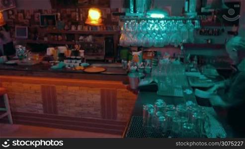 Timelapse of bar workers at work: barman is swinging lamps over the counter and making cocktails, waitress is serving them and working with check till