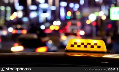 Timelapse of defocused city traffic at night with static yellow taxi sign on the car in the foreground. Copyspace from left