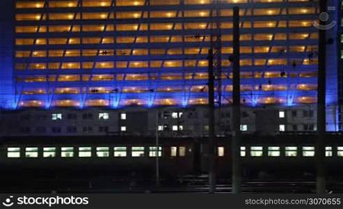 Timelapse of electric train passing by the lighted building in the city at night