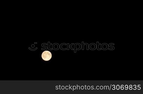 Timelapse of full moon moving against black night sky