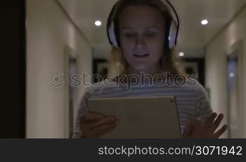 Timelapse of happy young woman listening to music in wireles earphones and using touch pad while walking in hotel hallway. Relaxing and leisure time