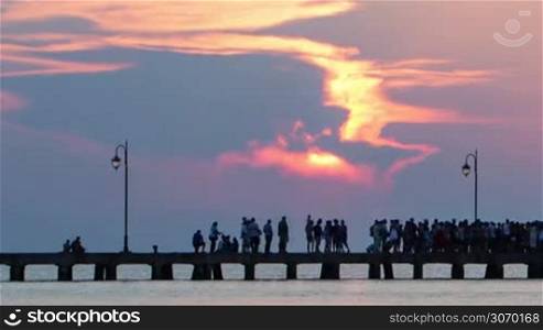 Timelapse of many people walking on pier and evening sun going down among the clouds