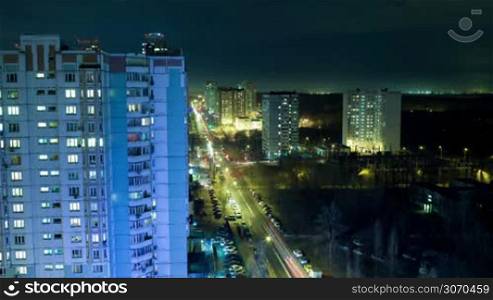 Timelapse of night city life with twinkling lights in windows of houses and intense traffic