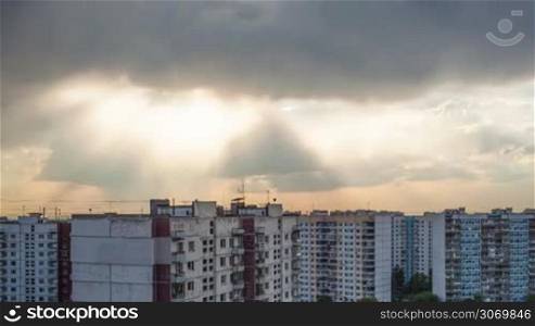 Timelapse of sky with dark heavy clouds hiding sun during sunset over city block of houses
