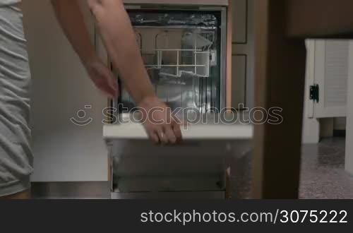 Timelapse of unseen woman putting dirty dishes and cutlery into dishwasher and turning it on