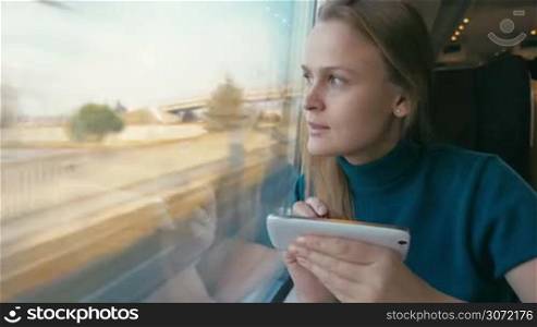 Timelapse of young woman traveling by rail. She typing text message on the phone with a pen and looking out the window