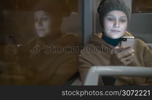 Timelapse of young woman typing text message on the phone while traveling in the night city by bus