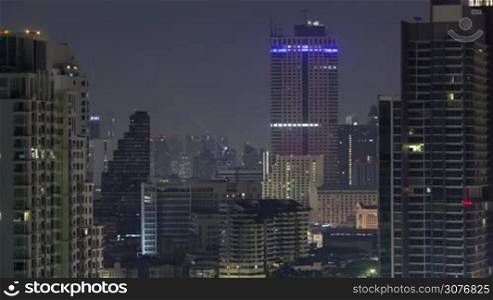 Timelapse shot of blinking windows and city lights of high-rise buildings in night Bangkok, Thailand