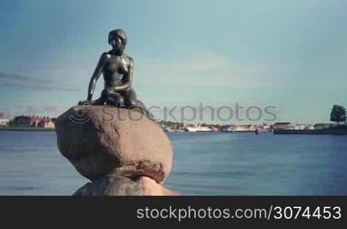 Timelapse shot of boats and ships sailing on the water behind the Little Mermaid statue, some tourists taking picture with it
